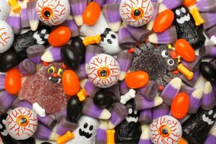 red veiny eyeballs with orange corneus and black pupils lay scattered along with ghosts, orange and black jelly beans and black spider gummies on a purple background.