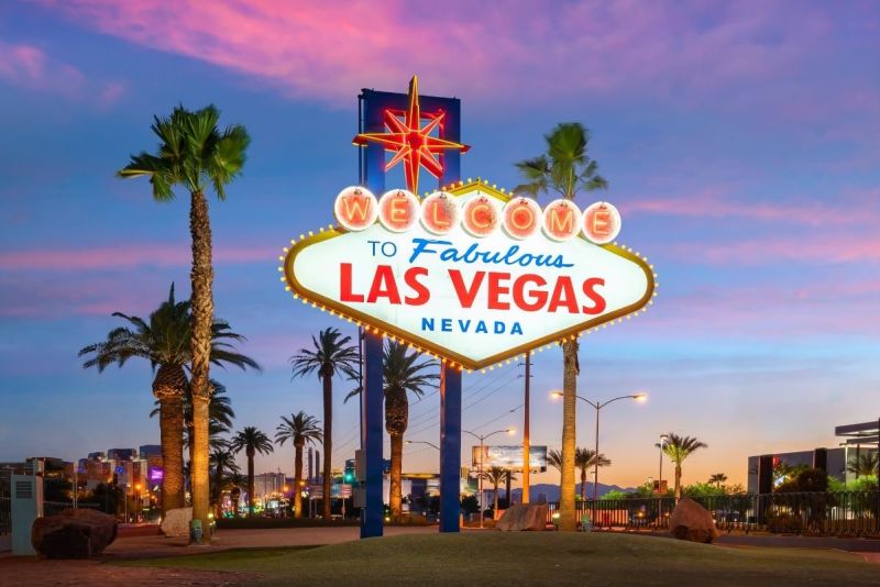 The iconic “Welcome to Fabulous Las Vegas” sign glowing at sunset with palm trees and a vibrant pink sky.