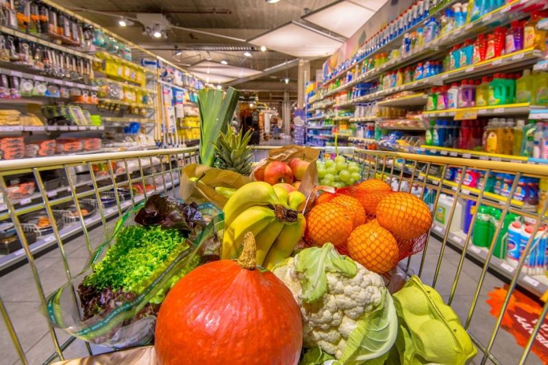 Grocery cart filled with colorful fruits and vegetables in a supermarket aisle.