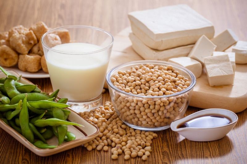 Soybeans, tofu, edamame, soy milk, and soy sauce arranged on a wooden table.