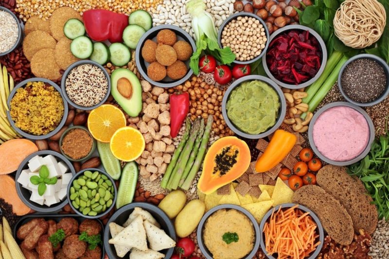 Colorful assortment of plant-based foods including vegetables, fruits, legumes, nuts, seeds, and grains.