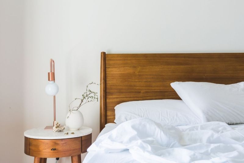 Minimalist bedroom with white bedding and a wooden headboard.