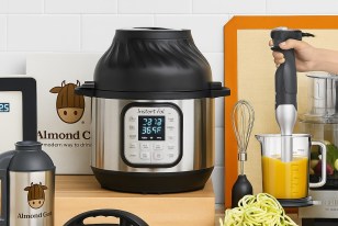 A modern kitchen countertop displays a variety of vegan kitchen gadgets, including a food processor, cutting board, olive oil, vegetables, and crispy tostadas, evoking a clean and plant-based cooking space.